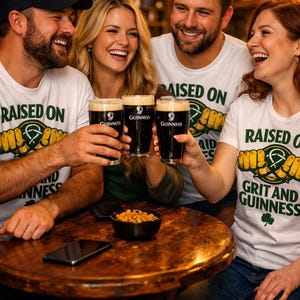 May include: Four people in a pub, smiling and toasting with pints of Guinness. They wear white t-shirts with the text "RAISED ON GRIT AND GUINNESS". A bowl of snacks and a phone sit on the wooden table. The image has the text "FRIENDS IN THE PUB".