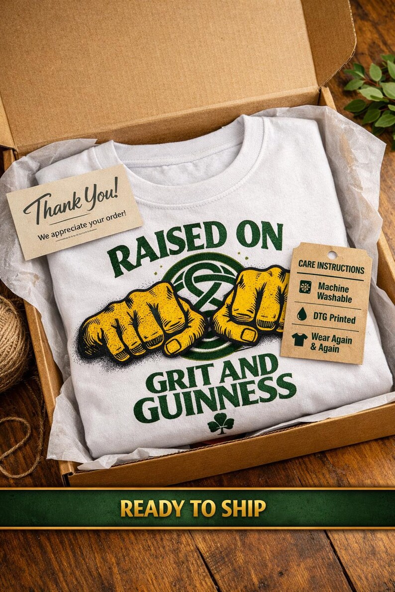 May include: A white t-shirt with the text "RAISED ON GRIT AND GUINNESS" in green, featuring a graphic of two yellow fists. The shirt is inside a cardboard box with a "Thank You" card and a care instructions tag.