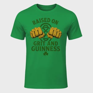 May include: Green t-shirt with the text "RAISED ON GRIT AND GUINNESS" in brown. The design includes two fists, a Celtic knot, and a shamrock. The shirt is a solid green color.