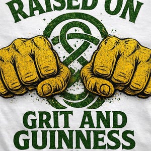 May include: White t-shirt with a green and yellow graphic. The design features two clenched fists, a Celtic knot, and the words "RAISED ON GRIT AND GUINNESS" in green. The bottom of the shirt has the words "CELTIC DETAIL".