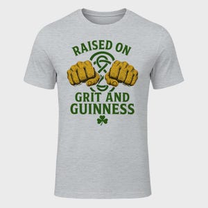 May include: A light gray t-shirt with the text "RAISED ON GRIT AND GUINNESS" in green. The design includes two fists, a Celtic knot, and a shamrock.
