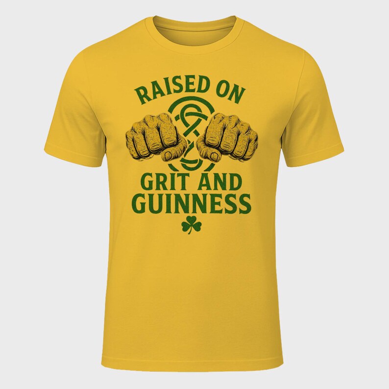 May include: Mustard yellow t-shirt with the text "RAISED ON GRIT AND GUINNESS" in green. The design includes two clenched fists, a Celtic knot, and a shamrock. The shirt is a short-sleeved crew neck.