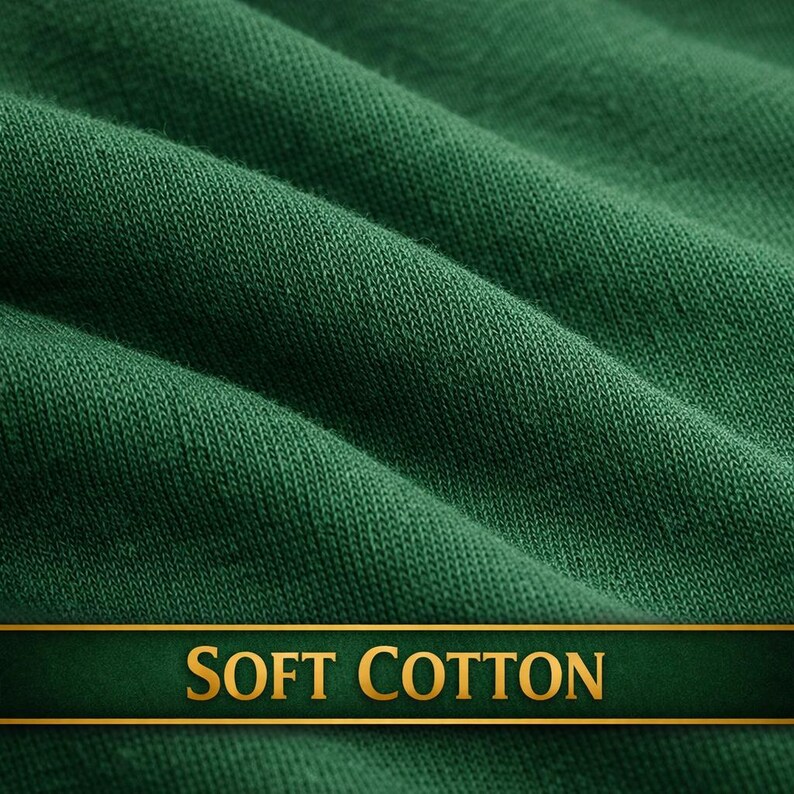 May include: Close-up of a textured, forest green fabric with soft folds. A dark green banner with gold lettering reads "SOFT COTTON". The fabric appears to be a knit or woven material, suggesting a textile product.