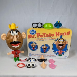 Könnte beinhalten: Ein Mr. Potato Head Spielzeug mit austauschbaren Gesichtsteilen, darunter Augen, Nasen, Münder und Hüte. Auf der Box steht "The Classic Funny-Face Kit!" und zeigt Illustrationen des Spielzeugs. Der Kartoffelkopf ist braun und trägt einen gelben Cowboyhut.