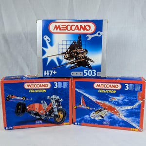 Könnte beinhalten: Drei Meccano-Konstruktionssets werden gezeigt, jedes in einer blauen Box mit dem Meccano-Logo. Die Sets enthalten Modelle eines Flugzeugs, eines Motorrads und eines Raumschiffs. Die Boxen haben die Nummern 503, 2950 und 2940.