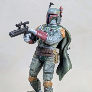 Pu&ograve; includere: Una dettagliata action figure di Boba Fett, personaggio di Star Wars. La figura &egrave; in posa di combattimento, con un fucile blaster. Presenta una combinazione di colori verde, rosso e grigio, con un mantello verde. La figura &egrave; molto dettagliata.