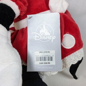May include: A plush toy dressed in a red and white Santa Claus outfit, with a Disney tag attached. The tag features the Disney logo and product information.