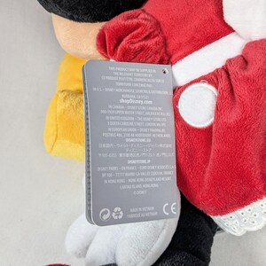 May include: A plush Minnie Mouse doll with a red dress, white trim, and black gloves. The doll has a tag with text in English and French. The doll is a Disney product.