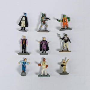 May include: A set of ten Star Wars action figures, including characters such as Boba Fett, a green alien, and a blue-skinned figure. The figures are all small and made of plastic, and they are standing on small grey bases.