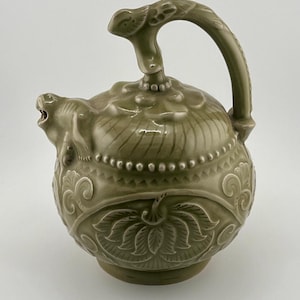 May include: A green ceramic teapot with a dragon spout and a floral design. The teapot has a unique handle shaped like a dragon.