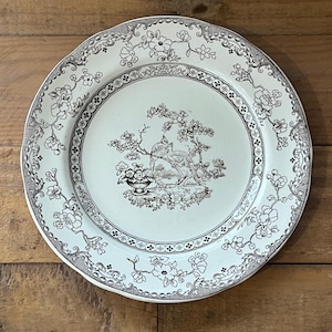 May include: A white ceramic plate with a black and white floral design. The centre of the plate features a black and white illustration of two birds perched on a branch.
