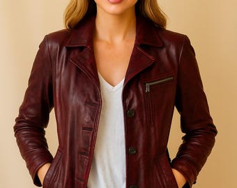 May include: A burgundy leather jacket with a notched collar, button closure, and a zippered chest pocket. The jacket has two front pockets and is worn over a white v-neck shirt. The model is wearing blue jeans.