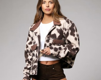 May include: A cropped cow print jacket with brown and cream spots, featuring a brown collar and pocket accents. The jacket is paired with brown shorts and a white top, creating a stylish ensemble.