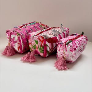 Op de afbeelding: Drie roze quilted stoffen tasjes met bloemenpatronen en kwastjes. De tasjes zijn van verschillende grootte en zijn gerangschikt in een rij van groot naar klein.