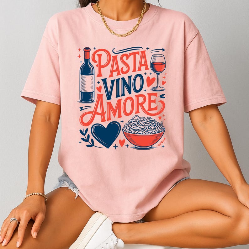 May include: A light pink t-shirt with the words "Pasta Vino Amore" in red and blue script. The design includes a wine bottle, a glass of wine, a bowl of pasta, and a blue heart.