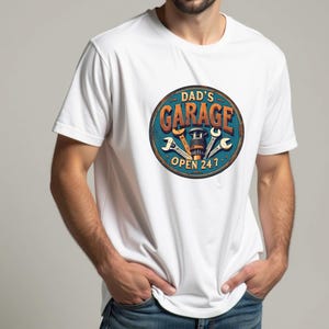 Może przedstawiać: Biała koszulka z niebiesko-pomarańczową grafiką klucza i tekstem "Garage Taty Otwarte 24/7".