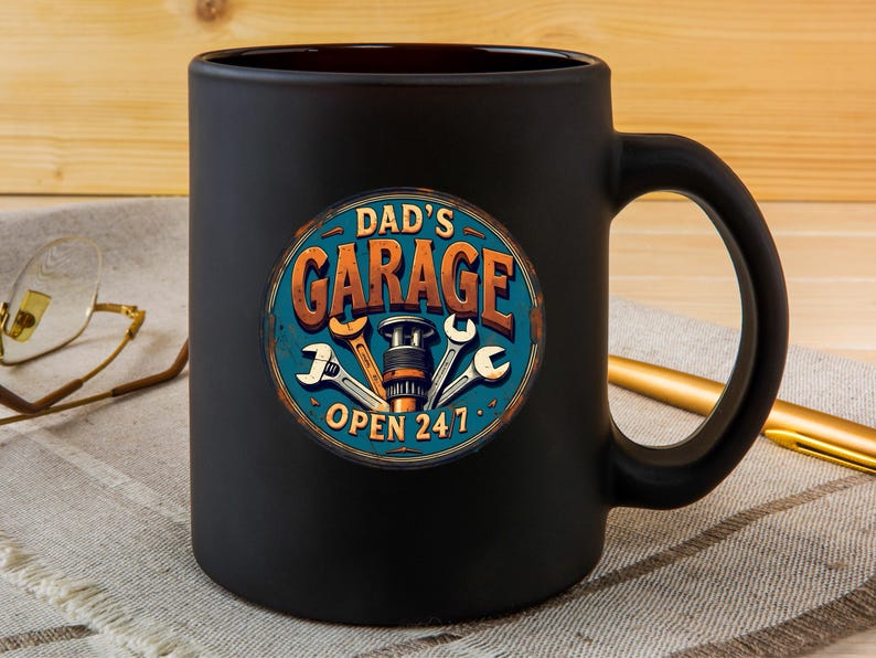 Może przedstawiać: Czarny ceramiczny kubek do kawy z grafiką vintage'owego znaku z napisem "Garage Taty Otwarty 24/7" z narzędziami i częścią samochodową w środku.