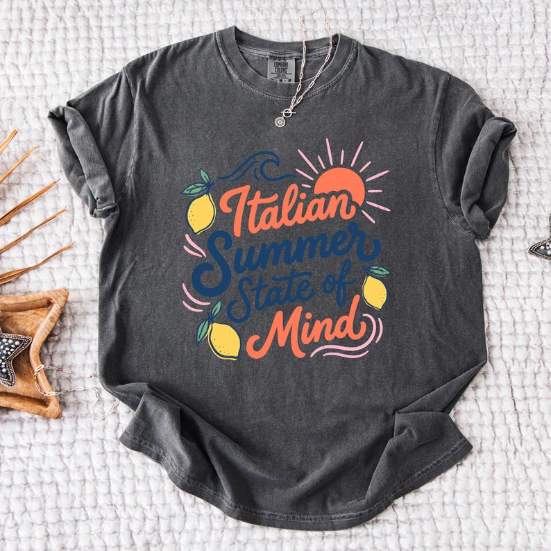 May include: Dark gray t-shirt with the text "Italian Summer State of Mind" in orange and blue. The design includes lemons, a sun, and waves. A silver necklace is visible.