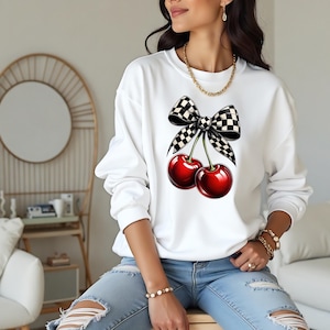 May include: White sweatshirt featuring a black and white chequered bow and two red cherries.