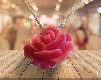 May include: A pink rose pendant necklace. The pendant is a detailed, three-dimensional rose with a silver-colored chain. The rose is a vibrant pink color, and the necklace is displayed on a wooden surface.