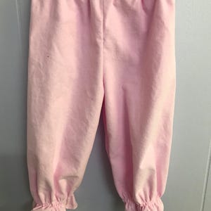 May include: Light pink corduroy pants featuring an elasticized waistband and gathered, ruffled cuffs at the bottom of each leg. The fabric has a distinct vertical ribbed texture throughout, providing a consistent solid color appearance.