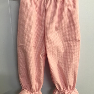 May include: Pink gingham baby pants with elastic waistband and ruffled hems.