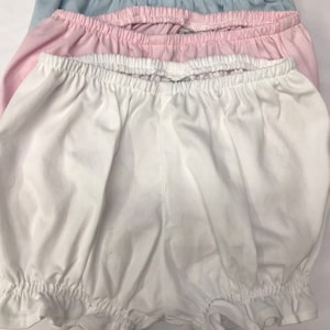 May include: Three pairs of cotton bloomers in white, pink, and light blue. The bloomers have a ruffled hem and are made of a soft, stretchy fabric.