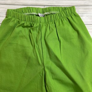 May include: Bright green pants with an elastic waistband. The fabric has a subtle texture. The pants are a solid color and appear to be made of a comfortable material. The pants are suitable for casual wear.