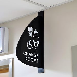 May include: Black and white sign with the text "CHANGE ROOMS" and symbols for toilet, shower, wheelchair, female, and transgender.