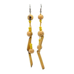 May include: A pair of dangle earrings featuring a combination of natural wood and yellow accents. The earrings have a silver hook, with a design that includes wooden beads, small yellow beads, and elongated wooden pieces. The earrings are designed to hang down.