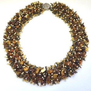 May include: A handcrafted necklace featuring a mosaic of brown, amber, and cream-colored beads. The beads are clustered together, creating a textured surface. The necklace is secured with a silver-colored clasp. The overall design is organic and earthy.