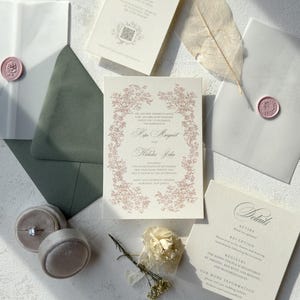 May include: Elegant wedding invitation suite featuring a floral design in blush pink. Includes invitation cards, RSVP cards, details card, envelopes with wax seals, and a ring box. The suite is arranged on a white surface with dried flowers.