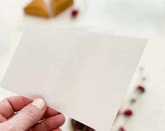 May include: A blank white card held in a hand, with a blurred background of a wooden triangle and a red berry.