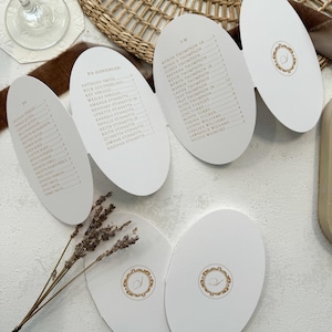 May include: A white wedding seating chart with gold lettering. The chart is divided into two sections, one for the groom's side and one for the bride's side. The groom's side is labeled "T.W." and the bride's side is labeled "P.A.". The chart lists the names of the guests in alphabetical order.