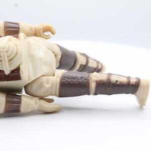 May include: A vintage Star Wars action figure of a Sandtrooper, lying on its side. The figure is made of plastic and has a brown and white color scheme. The figure has a backpack and a blaster rifle. The figure is marked with the copyright "&copy;1980 LFL" and "&copy;1980 Kenner".