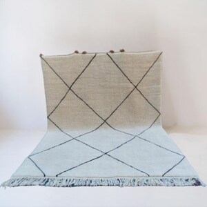 Può includere: Un tappeto marocchino bianco e azzurro con un motivo a rombi neri. Il tappeto ha un bordo a frangia.