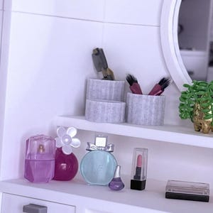 May include: A miniature vanity scene with perfume bottles, lipstick, and decorative containers. The bottles are various shapes and colors, including pink, purple, and blue. A small potted plant and a mirror are also visible.