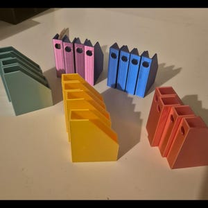 May include: Set of six colorful, 3D printed, angled bookends. The bookends are in shades of blue, pink, yellow, and green.