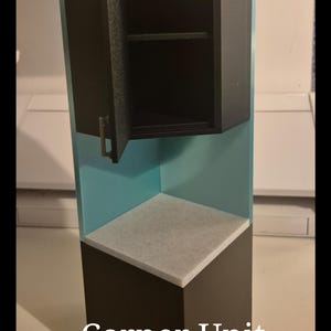May include: A miniature corner unit with a black cabinet and a light blue interior. The cabinet door is open, revealing a shelf. The base is dark brown with a white countertop. The text "Corner Unit" is at the bottom.