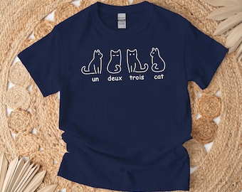 May include: A navy blue t-shirt with a white graphic of three cats and the text "un deux trois cat".