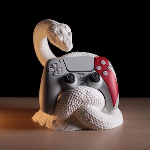 Könnte beinhalten: Ein grauer und roter Videospiel-Controller liegt auf einer weißen, strukturierten Skulptur einer Schlange. Der Controller hat eine graue Mitte und rote Akzente. Die Schlangenskulptur ist mit Schuppen und einem gewundenen Körper detailliert.