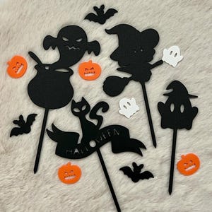 Könnte beinhalten: Eine Sammlung von Halloween-Dekorationen. Enthält schwarze Silhouetten einer Hexe auf einem Besen, eines Geistes, eines Kessels, einer Katze mit einem Banner mit der Aufschrift "Halloween", Fledermäuse und orangefarbene Kürbis-Ausschnitte. Weiße und orangefarbene Akzente.