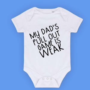 Puede incluir: Un body blanco para bebé con texto negro que dice "My Dad's Pull Out Game Is Weak."