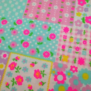 May include: A patchwork fabric with a repeating floral pattern. The fabric features squares of various colors, including pink, blue, and white. Each square is decorated with flowers in shades of pink, yellow, and blue. Some squares have polka dots.