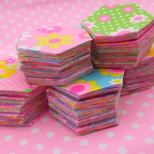 May include: A stack of pink, green and blue fabric hexagons with floral patterns. The hexagons are stacked on top of each other, creating a colourful and textured display.