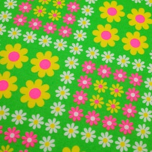 Può includere: Un tessuto verde con un motivo ripetitivo di fiori gialli e rosa. I fiori hanno una forma di margherita con un centro rosa e petali gialli.