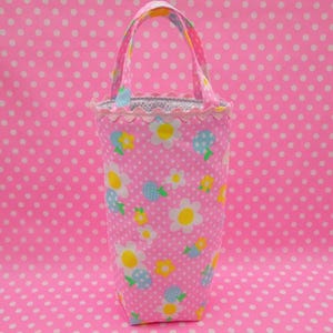 Puede incluir: Una bolsa de tela rosa con un patrón de lunares blancos y un estampado floral. La bolsa tiene un borde festoneado y un asa rosa.