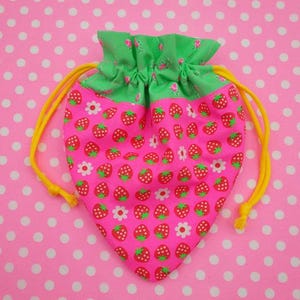 May include: A pink drawstring bag with a strawberry print and a green top. The bag has yellow drawstrings.
