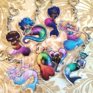 Op de afbeelding: Een verzameling kleurrijke zeemeermin sleutelhangers. Elke sleutelhanger heeft een uniek zeemeerminontwerp met levendige haren en staarten in tinten blauw, paars, roze en groen. De sleutelhangers hebben zilverkleurige hartvormige sluitingen.