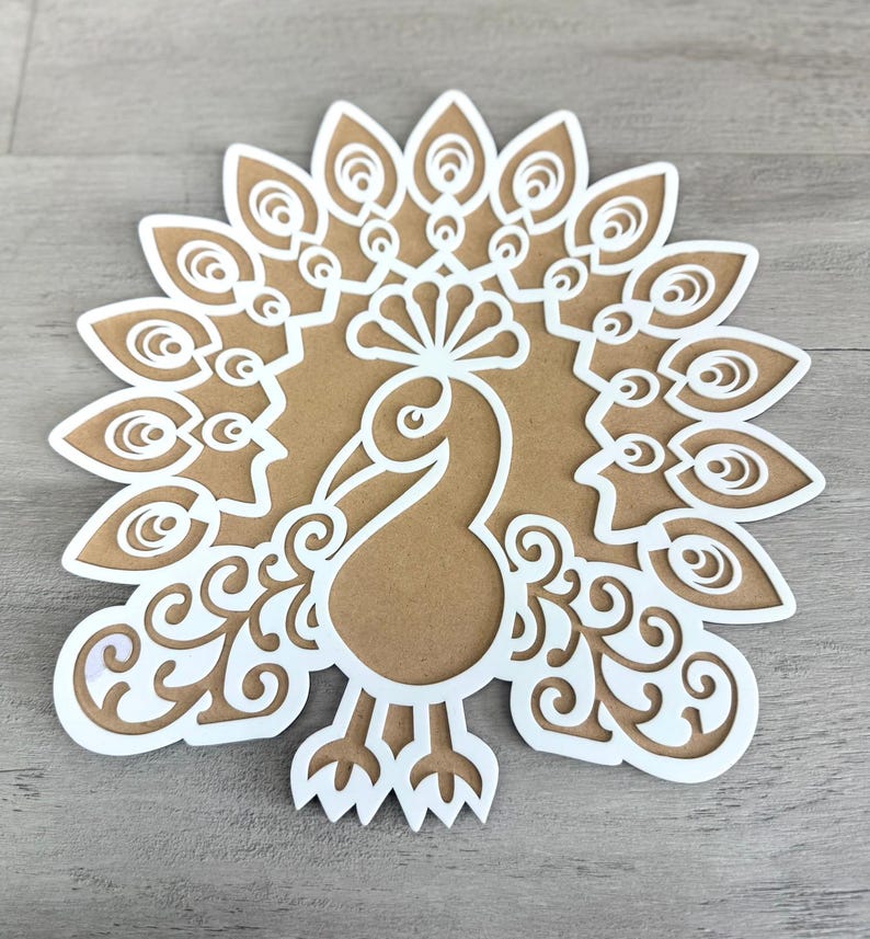 May include: A white paper cut-out of a peacock with a detailed design. The peacock is facing forward with its tail feathers spread out behind it.